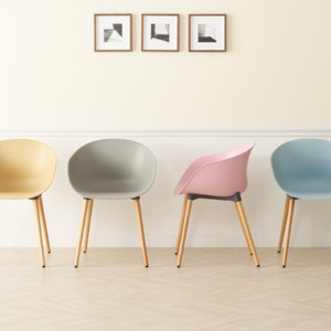 A row of four Lismark modern dining chairs with moulded plastic seats in pastel yellow, grey, pink, and light blue, each with natural wood-effect legs, set against a light wall with three framed geometric art prints.
